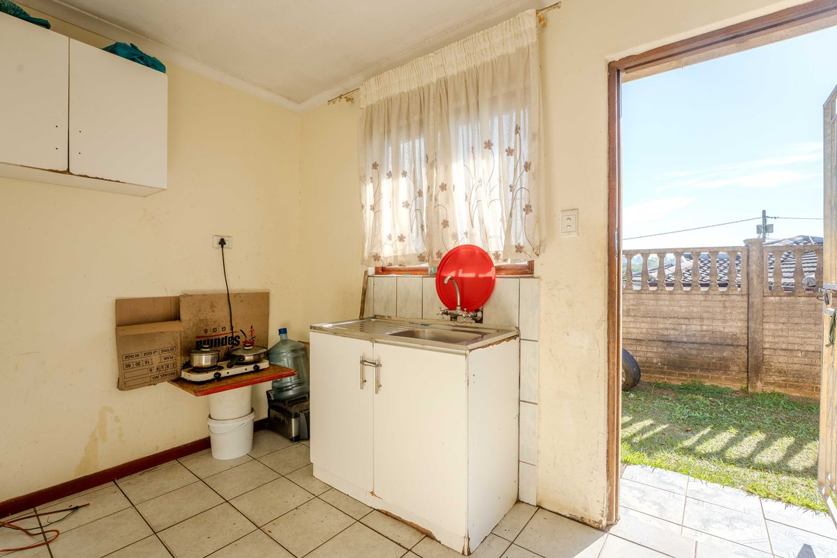A compact kitchen area featuring a single basin sink, tiled splashback, and direct access to the rear garden through an external door.