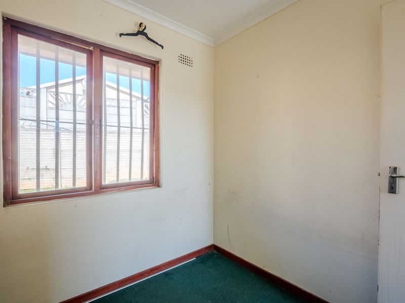An empty bedroom featuring carpet flooring, a timber-framed window with security bars, and neutral walls requiring cosmetic attention.