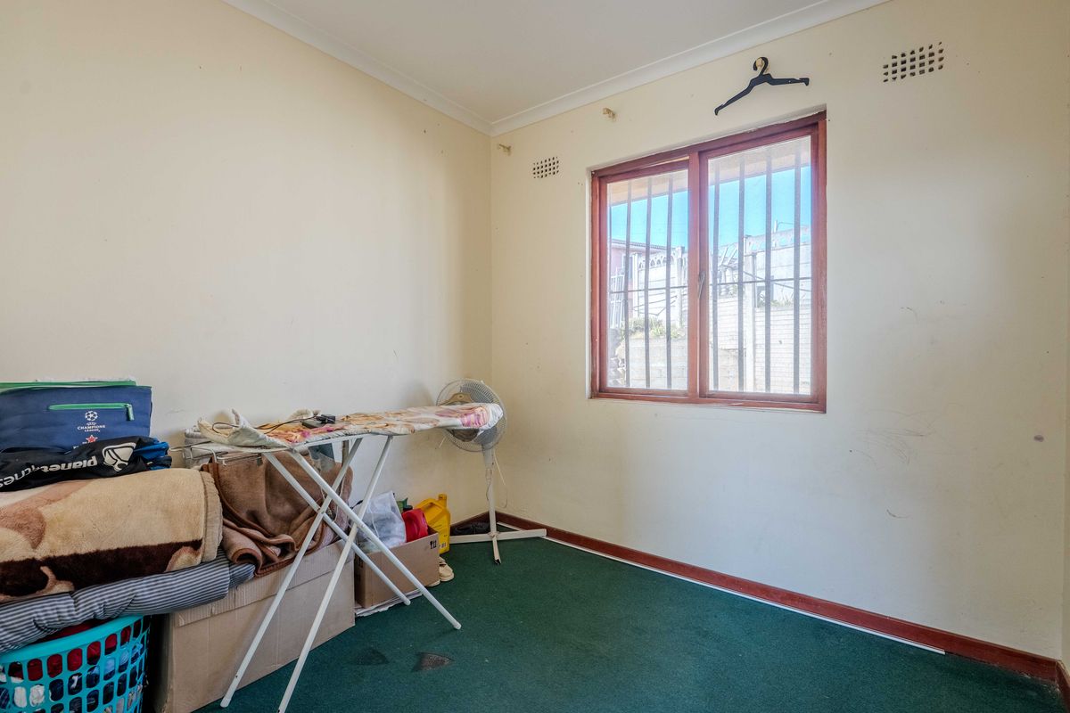 A bedroom featuring green carpet flooring, a window with security bars, and coved ceilings, requiring cosmetic updates to the walls and flooring.