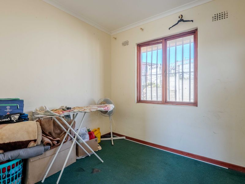 A bedroom featuring green carpet flooring, a window with security bars, and coved ceilings, requiring cosmetic updates to the walls and flooring.