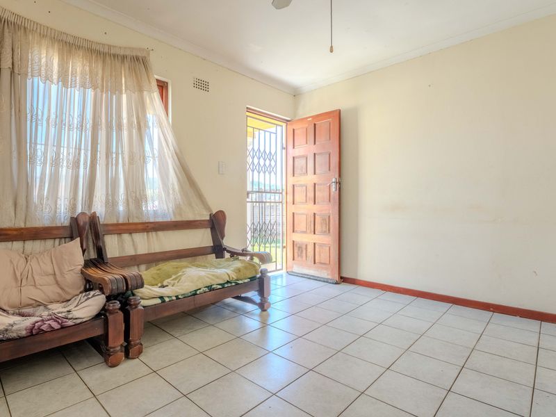A living area featuring tiled flooring, a timber entrance door with security gate, and a ceiling fan, offering a functional space with potential for updates.