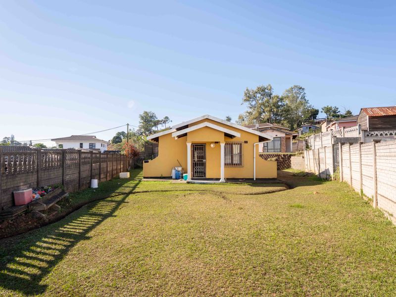 Rear view of a detached house featuring a spacious lawn, enclosed by precast concrete boundary walls and a secure entrance gate.