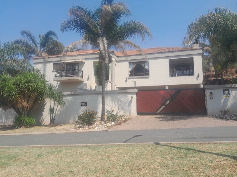 Front elevation of a double-story house featuring a paved driveway, large sliding gate, balcony, and established perimeter wall with security fencing.