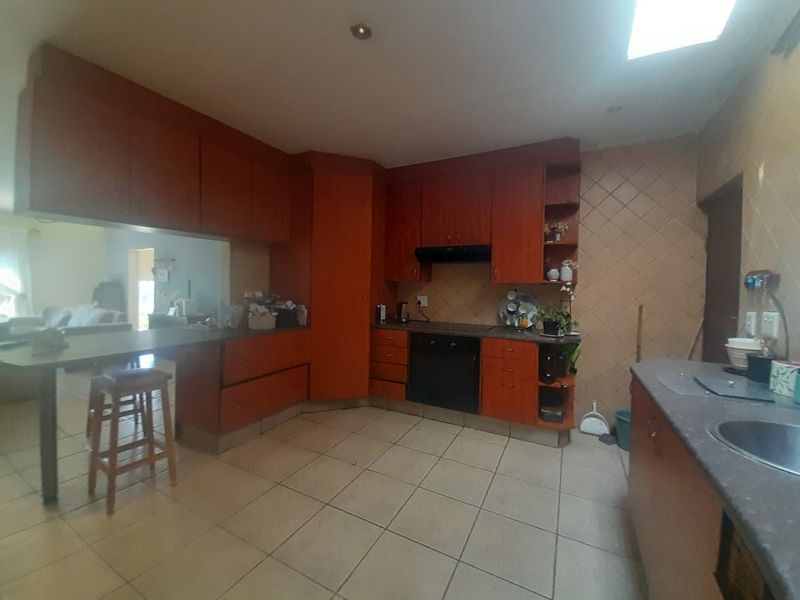 A functional kitchen featuring wooden cabinetry, built-in oven with extractor, tiled flooring, and a breakfast bar overlooking the adjacent living area.
