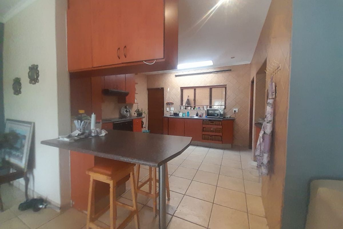 A dated kitchen featuring wood-tone cabinetry, laminate countertops, and ceramic floor tiles, including a built-in breakfast bar and functional workspace.