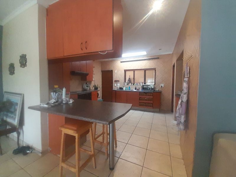A dated kitchen featuring wood-tone cabinetry, laminate countertops, and ceramic floor tiles, including a built-in breakfast bar and functional workspace.