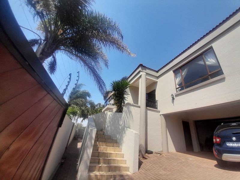 Front exterior view of the property featuring a paved driveway, covered garage space, and a tiled staircase leading to the main entrance.