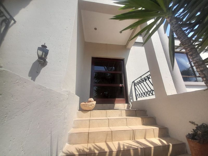 A welcoming front entrance featuring a tiled staircase, wrought iron railing, and a timber-framed glass door under a covered porch area.