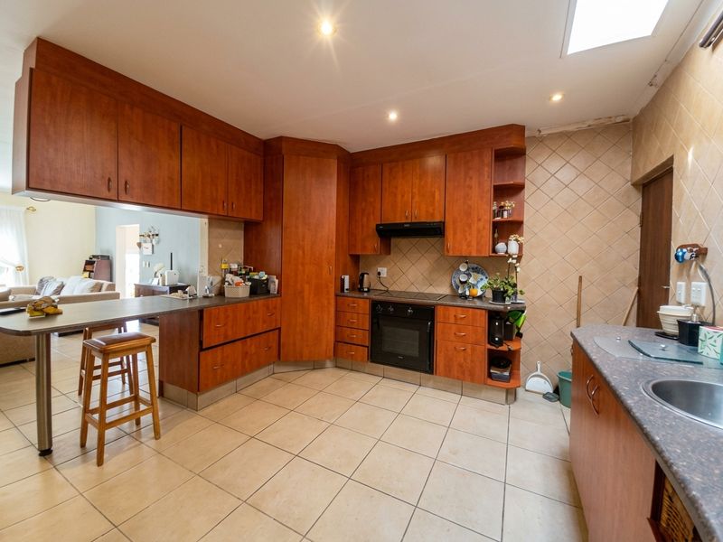 A functional kitchen featuring warm-toned wooden cabinetry, a breakfast bar, built-in oven, extractor fan, and tiled flooring with a skylight for natural illumination.