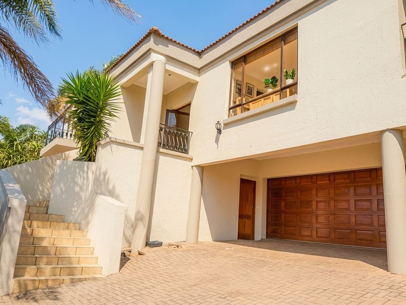 Front elevation of a multi-level residence featuring a paved driveway, integrated garage, and an elevated balcony with staircase access.