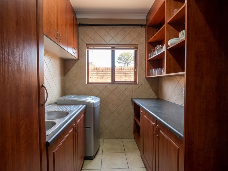 A functional laundry room featuring built-in wooden cabinetry, laminate countertops, a stainless steel sink, and tiled finishes.