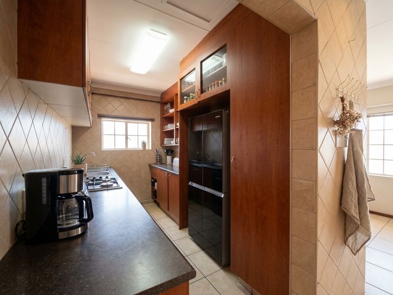 A functional kitchen featuring warm-toned wooden cabinetry, dark laminate countertops, a gas hob, and classic tiled finishes throughout.