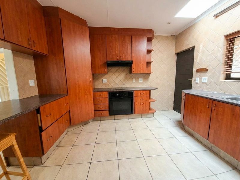 A functional kitchen featuring warm-toned wooden cabinetry, tiled flooring, a built-in oven with extractor fan, and a skylight providing natural light.