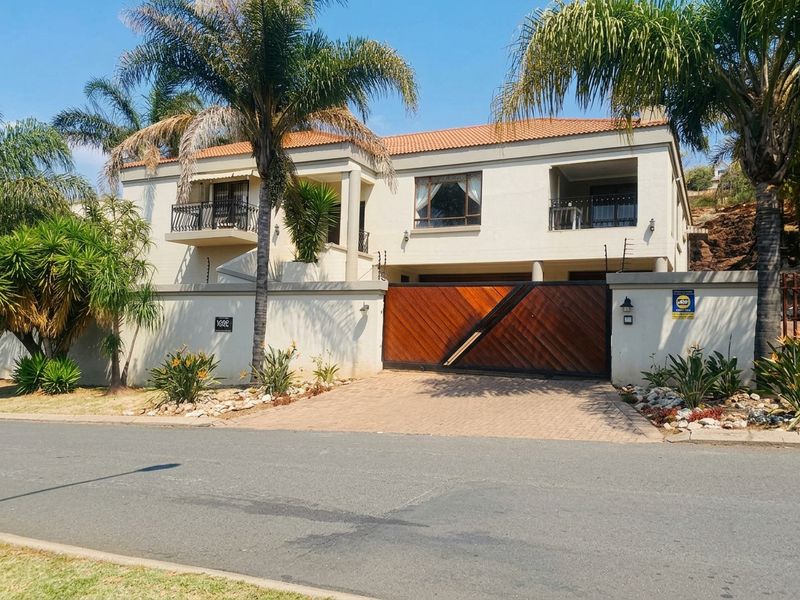 A well-maintained double-story residence featuring a paved driveway, secure wooden gate, electric fencing, and upper-level balconies with wrought iron railings.