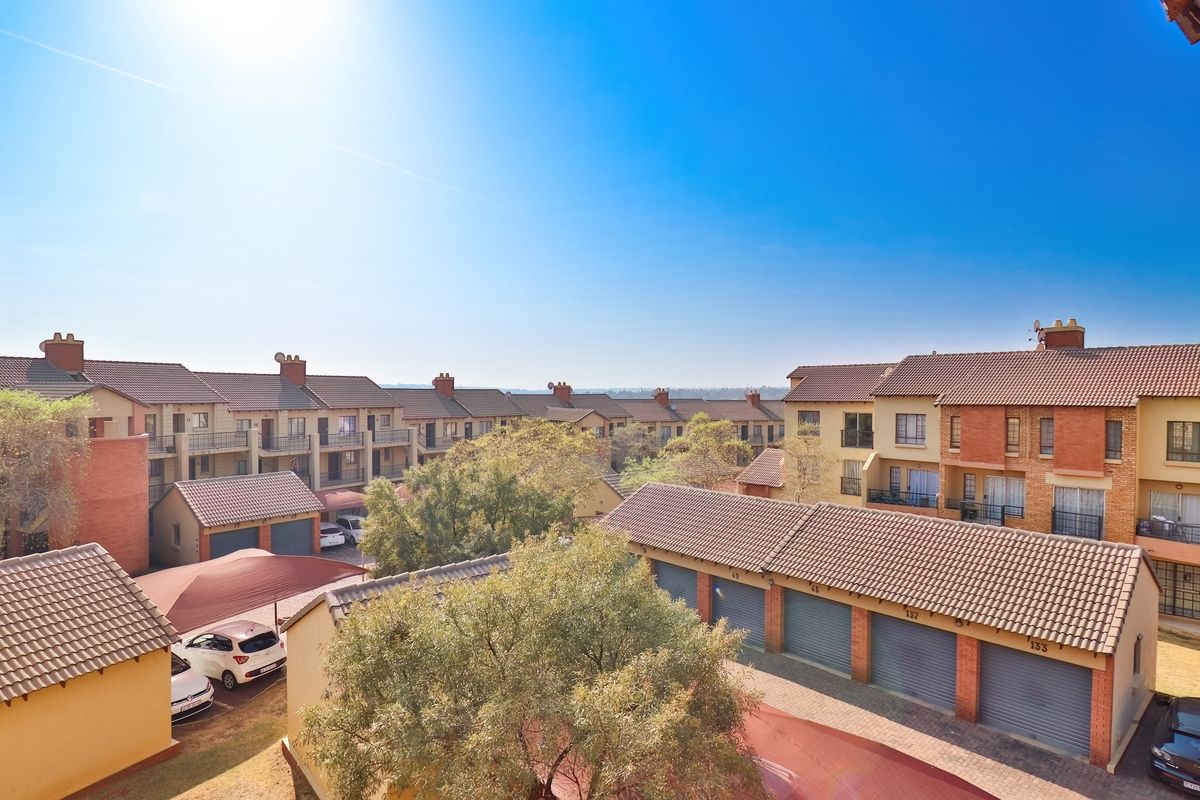 An elevated view of a residential apartment complex featuring multiple units with tiled roofs, brick facades, and a central paved parking area with carports.
