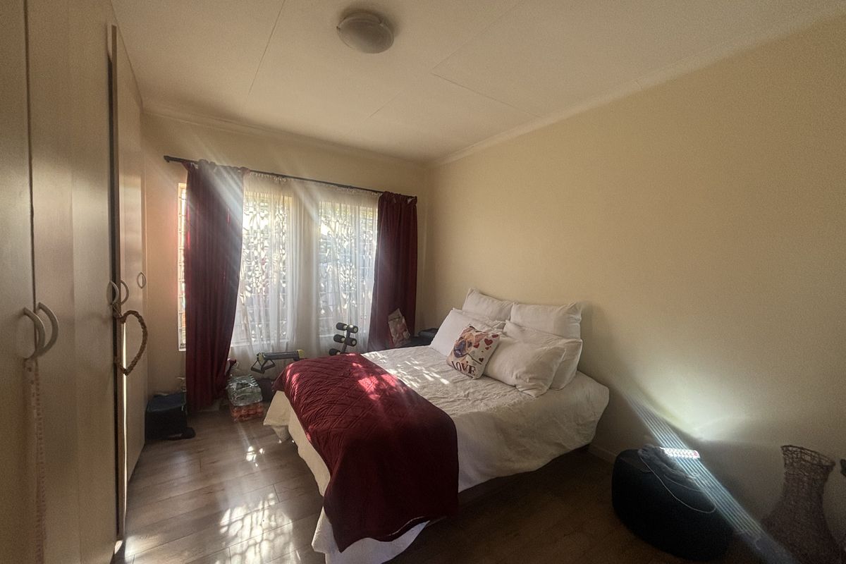 A functional bedroom featuring built-in cupboards, laminate flooring, and natural light through the window.