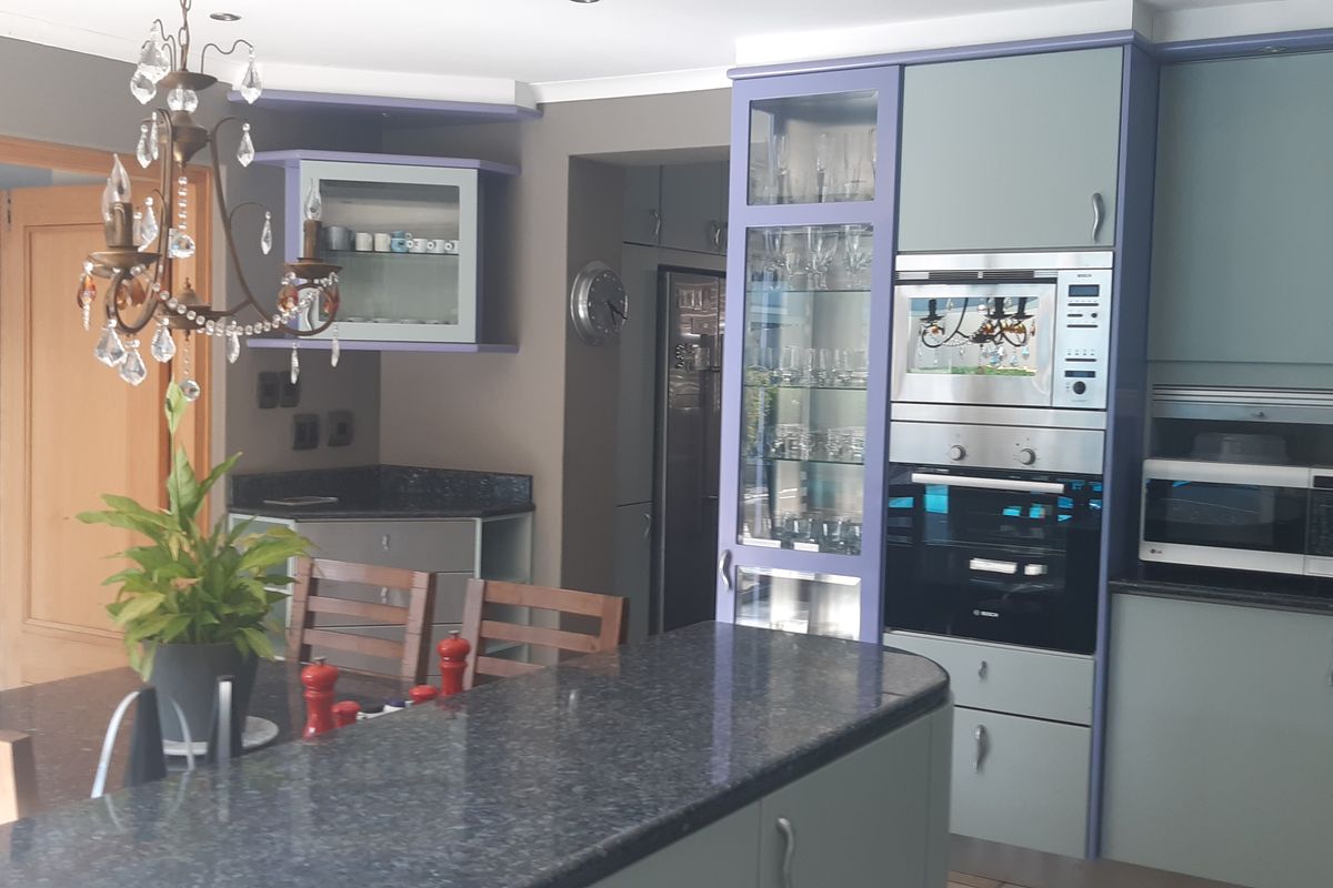 A functional kitchen featuring granite countertops, built-in appliances, and custom cabinetry with a mosaic tile backsplash, opening into an adjacent dining area.