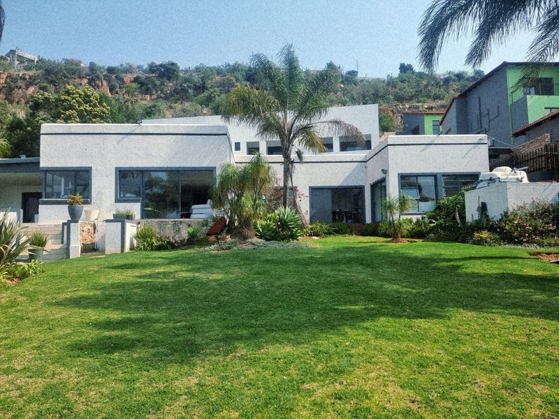Rear view of a modern white house featuring large sliding glass doors, expansive windows, and a well-maintained lawn and garden area.