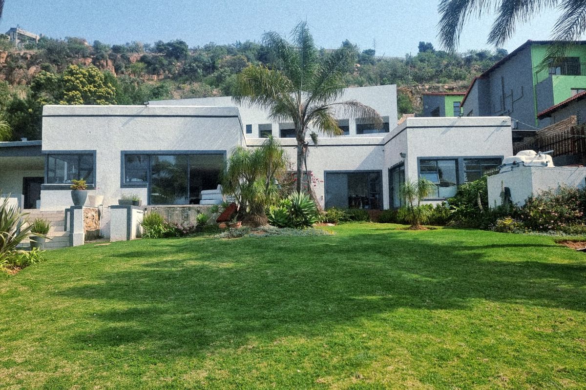 Rear view of a modern white house featuring large sliding glass doors, expansive windows, and a well-maintained lawn and garden area.