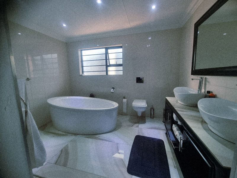 Modern bathroom featuring a freestanding bathtub, wall-mounted toilet, and a double vanity with vessel sinks, finished with neutral floor-to-ceiling tiling.