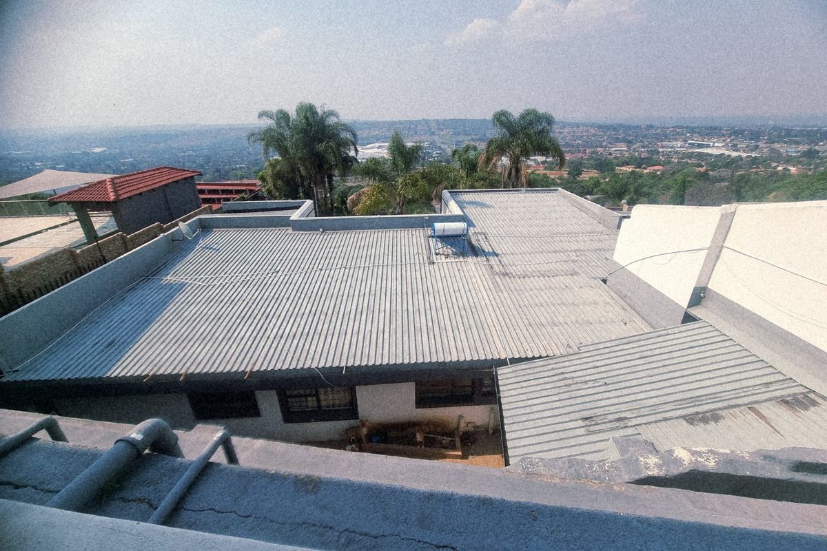 Aerial view of the property showing corrugated metal roofing, a solar water heating system, and surrounding residential landscape.