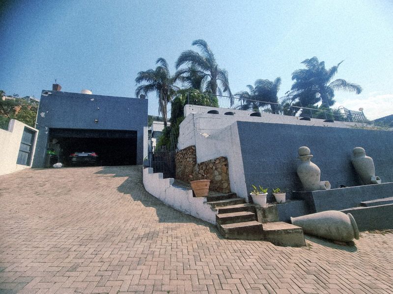 Front exterior view featuring a paved driveway, integrated garage, and tiered retaining walls with stone accents and concrete stairs.