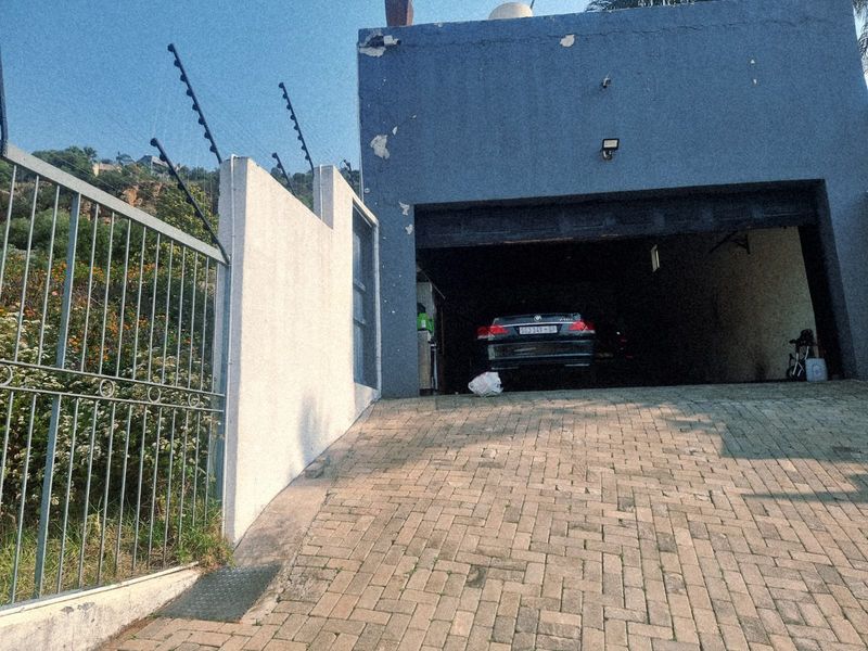 A view of a garage entrance with a paved driveway, perimeter wall, and electric fencing, showing signs of exterior wear.
