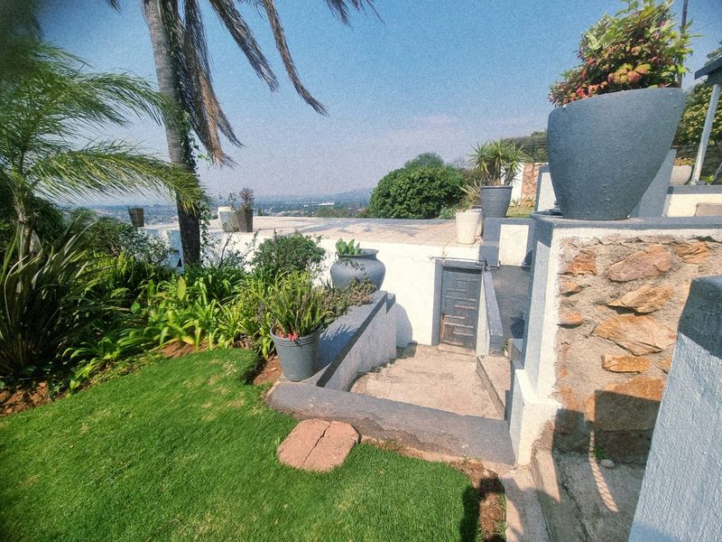 Rear exterior view featuring a landscaped garden, stone-clad retaining walls, and a concrete staircase leading to the lower level of the property.