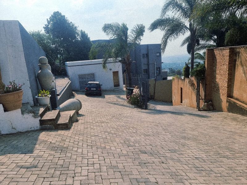 A paved driveway leading to the property entrance, featuring a brick boundary wall, security gate, and concrete steps.