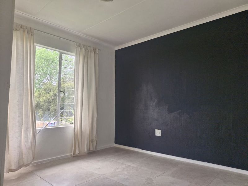 An empty bedroom featuring tiled flooring, a large window with security bars, and a dark accent wall with visible paint wear.