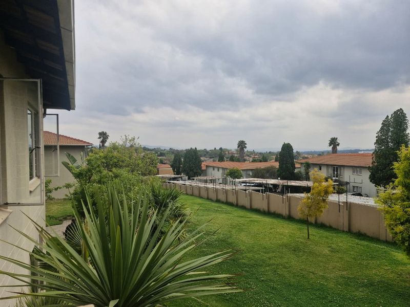An elevated view overlooking a communal garden area, perimeter boundary wall, and residential complex carports under a cloudy sky.