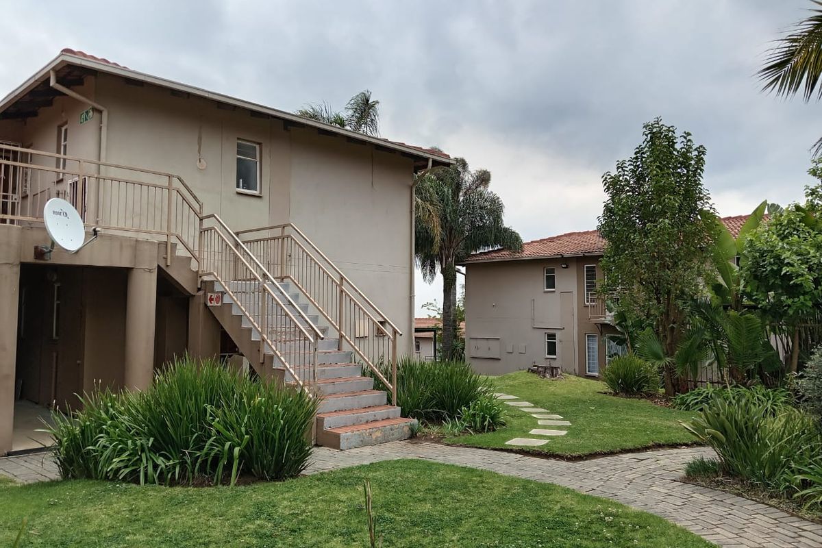 Exterior view of apartment complex featuring a metal staircase, paved garden pathways, and landscaped green areas.