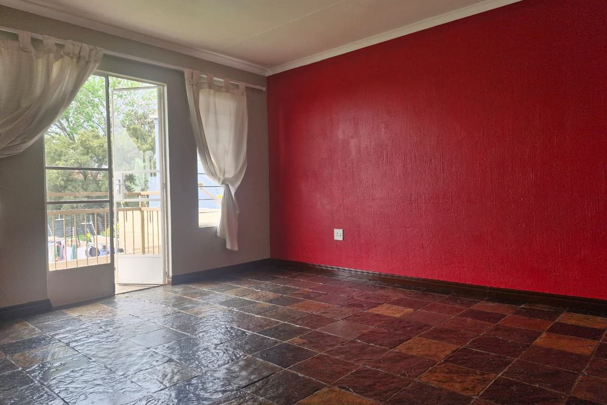 An empty living room featuring dark textured floor tiles, a bold red accent wall, and direct access to a balcony through a sliding glass door.