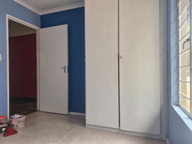 A bedroom featuring built-in cupboards, tiled flooring, and security bars on the window, presenting a clean, empty space ready for personalization.