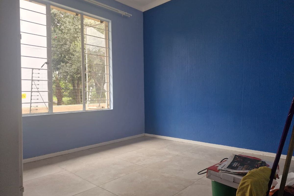 An empty bedroom featuring tiled flooring, blue accent walls, and large windows fitted with security bars.