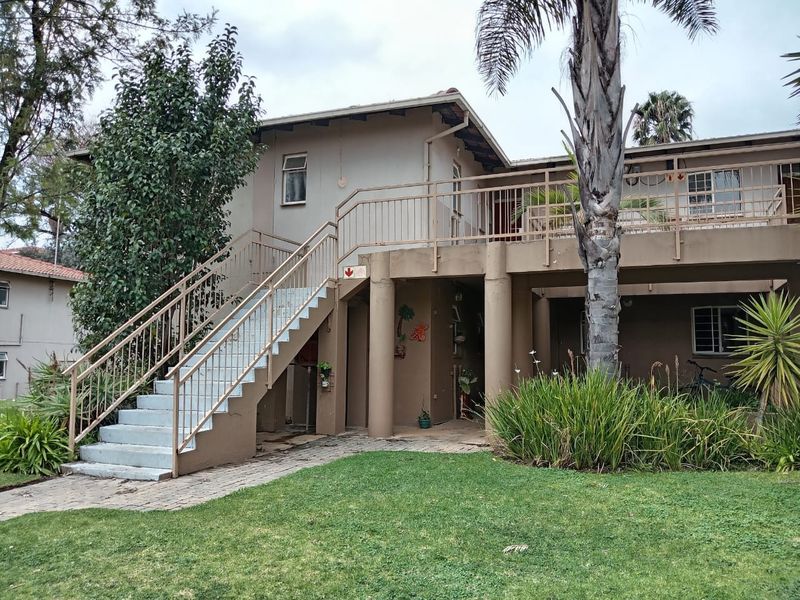 Rear view of the apartment building featuring an external staircase, raised balcony, and paved garden area with established landscaping.
