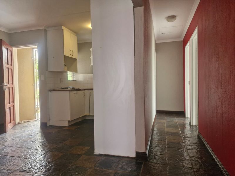 Open plan living area featuring tiled flooring, leading to a kitchen space and hallway with access to multiple rooms.