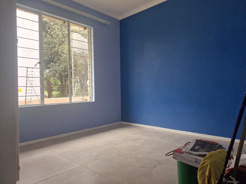 An empty bedroom featuring tiled flooring, blue accent walls, and large windows fitted with security bars.