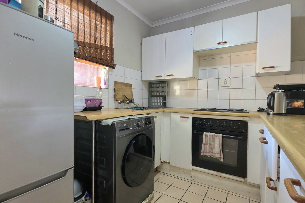 A compact kitchen featuring white cabinetry, laminate countertops, tiled backsplash, and built-in oven with hob, showing signs of wear and dated finishes.