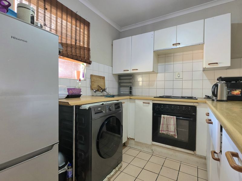 A compact kitchen featuring white cabinetry, laminate countertops, tiled backsplash, and built-in oven with hob, showing signs of wear and dated finishes.