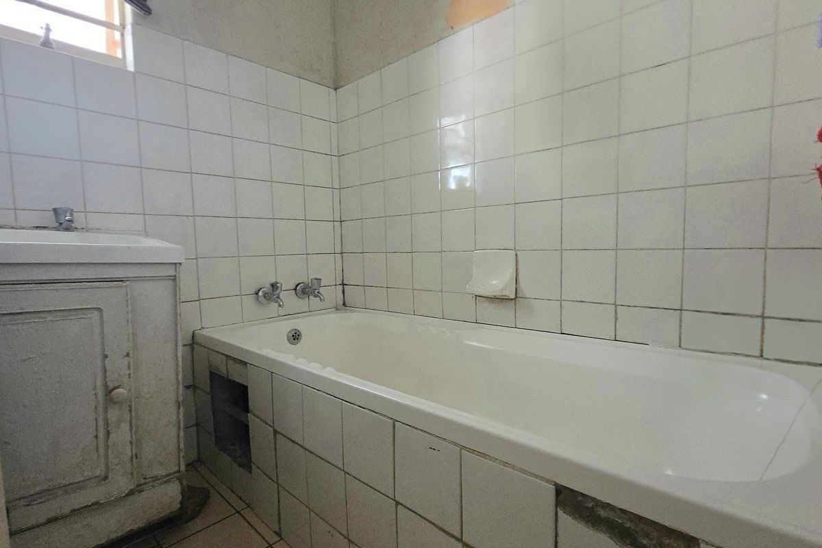 A dated bathroom featuring a built-in bathtub, vanity cabinet, and tiled surfaces, currently requiring cosmetic updates and repairs to the tile work.