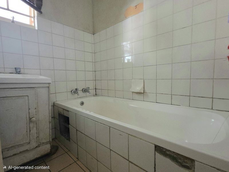A dated bathroom featuring a built-in bathtub, vanity cabinet, and tiled surfaces, currently requiring cosmetic updates and repairs to the tile work.
