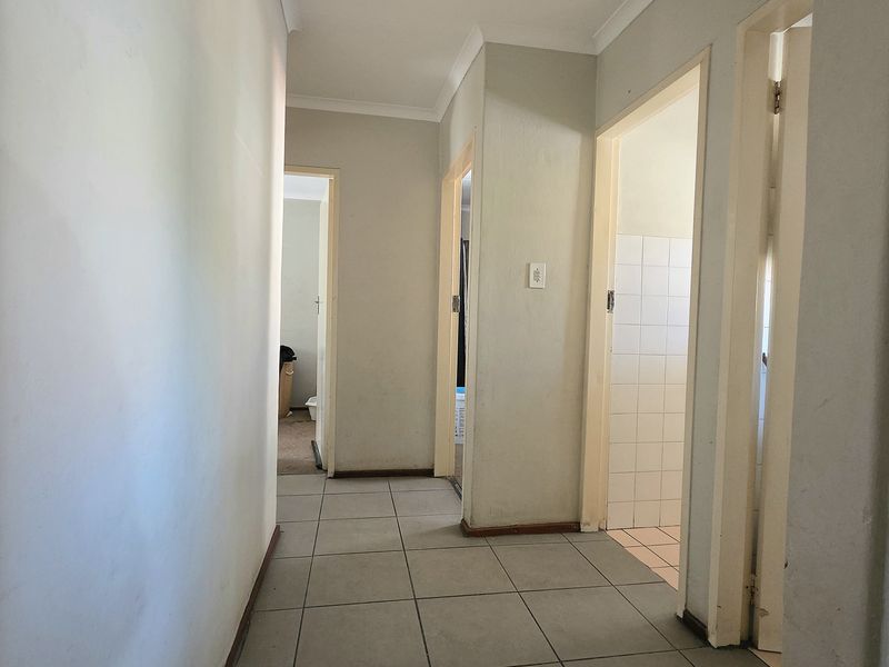 A functional hallway featuring neutral ceramic floor tiles and access to multiple rooms, showing signs of wear on walls and skirting boards.