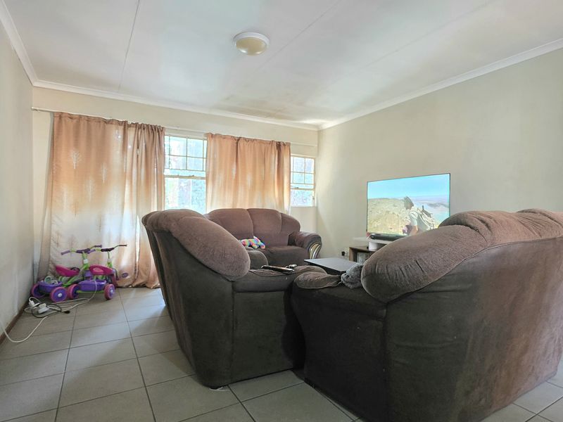 A living room featuring tiled flooring and coved ceilings, with visible water staining on the ceiling requiring attention.