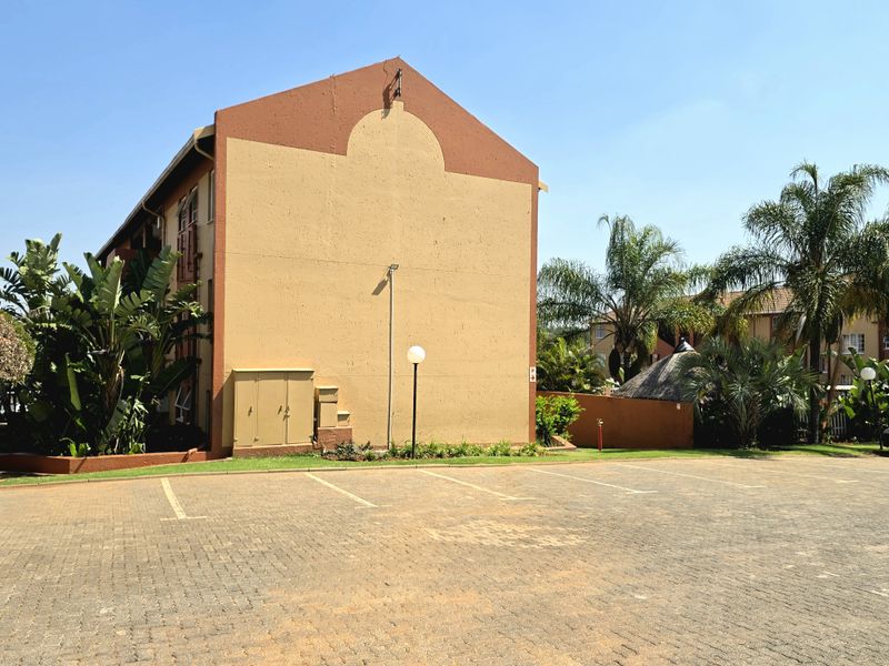 Exterior view of the townhouse complex featuring paved parking bays, landscaped garden areas, and well-maintained building facades.