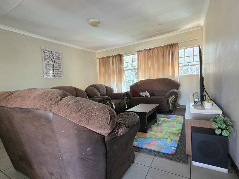 A living room featuring tiled flooring and ceiling lighting, showing signs of wear on the walls and ceiling that would benefit from cosmetic updates.