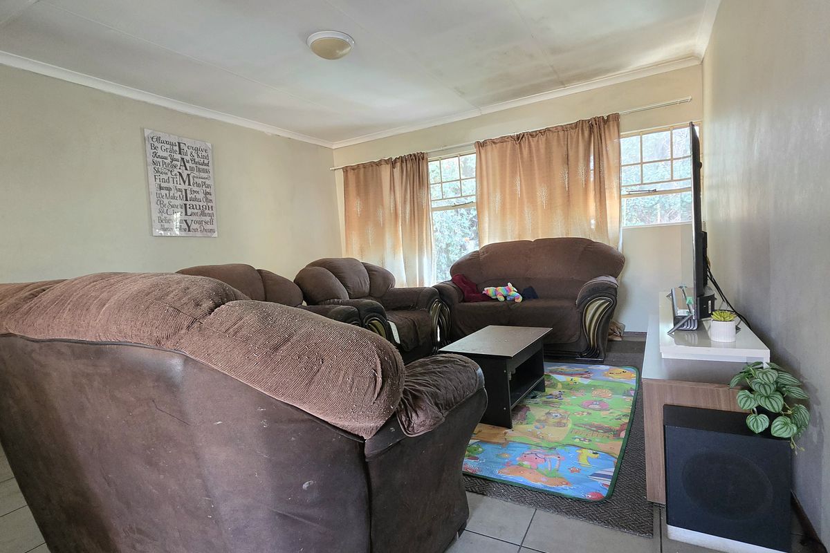 A living room featuring tiled flooring and ceiling lighting, showing signs of wear on the walls and ceiling that would benefit from cosmetic updates.