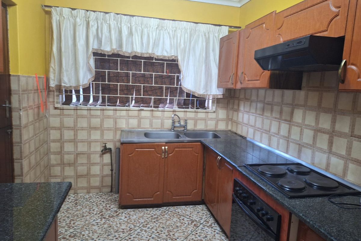 A functional kitchen featuring wooden cabinetry, granite countertops, a built-in oven with hob, and a double stainless steel sink with tiled splashbacks.