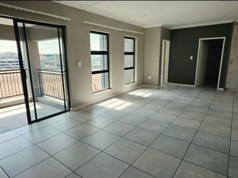 Spacious open-plan living area featuring neutral tiled flooring, recessed lighting, and direct access to a private balcony through large sliding glass doors.