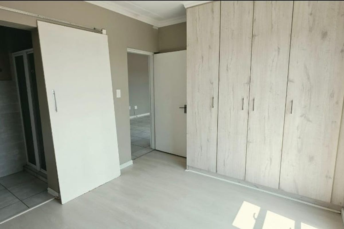 A bright, empty bedroom featuring light-toned laminate flooring, modern built-in cupboards, and a sliding door leading to an adjacent bathroom area.